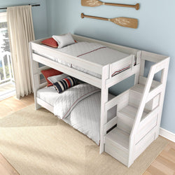 White wooden twin-over-twin bunk bed with built-in staircase storage in a coastal-style kids bedroom with striped pillows, white bedding, natural light and paddle wall decor