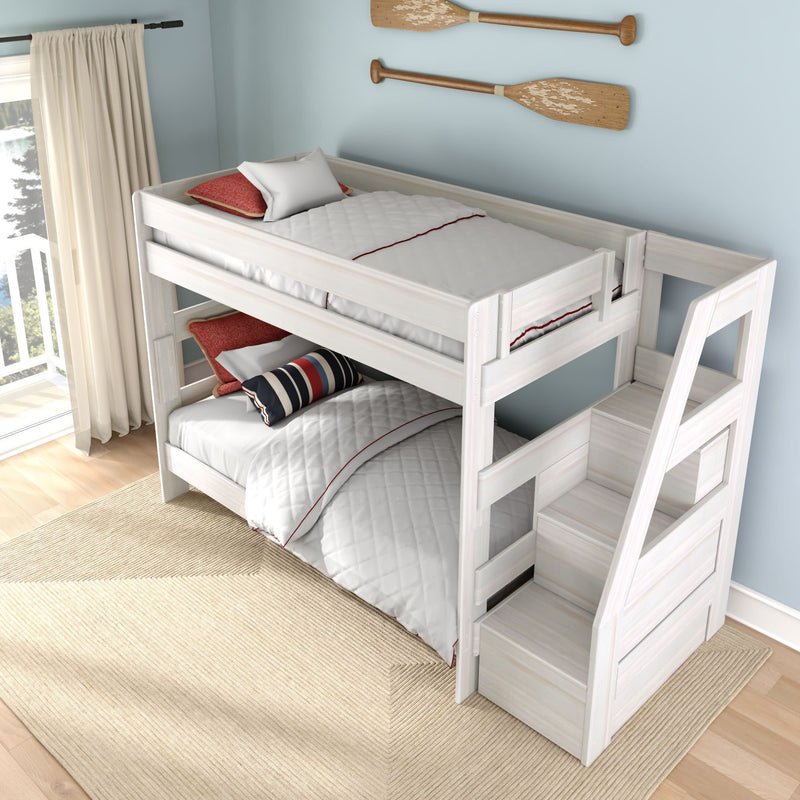 White wooden twin-over-twin bunk bed with built-in staircase storage in a coastal-style kids bedroom with striped pillows, white bedding, natural light and paddle wall decor