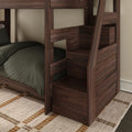 Dark walnut wooden bunk bed with built-in storage stairs and railing, lower twin bed with dark green bedding on a woven area rug — modern space-saving kids bedroom furniture