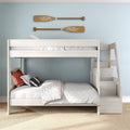 White wooden bunk bed with built-in storage stairs in coastal kids bedroom, light blue wall, quilted bedding and decorative wooden oars