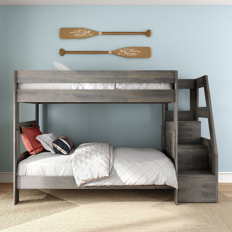 Kids gray wooden bunk bed with staircase storage, white quilted bedding and nautical pillows against a light blue wall with rustic wooden oars
