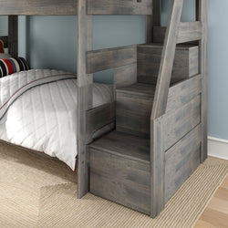 Gray wooden bunk bed with built-in storage staircase, white quilted comforter and striped pillow in a light blue kids' bedroom