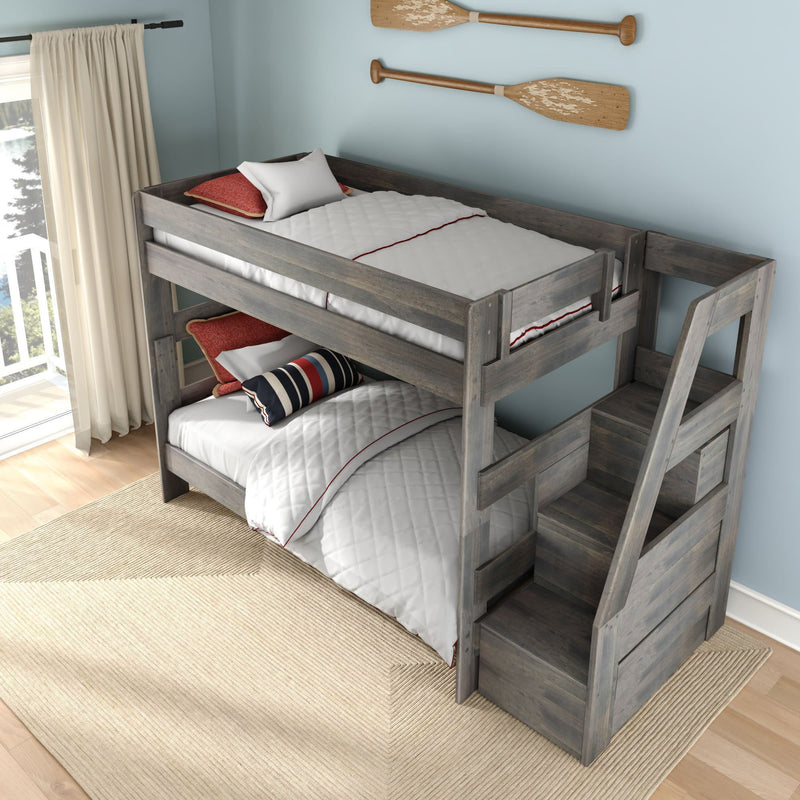 Graywashed wooden twin-over-twin bunk bed with built-in storage staircase, white quilted bedding, red accent pillows and nautical oar wall decor in a kids coastal bedroom