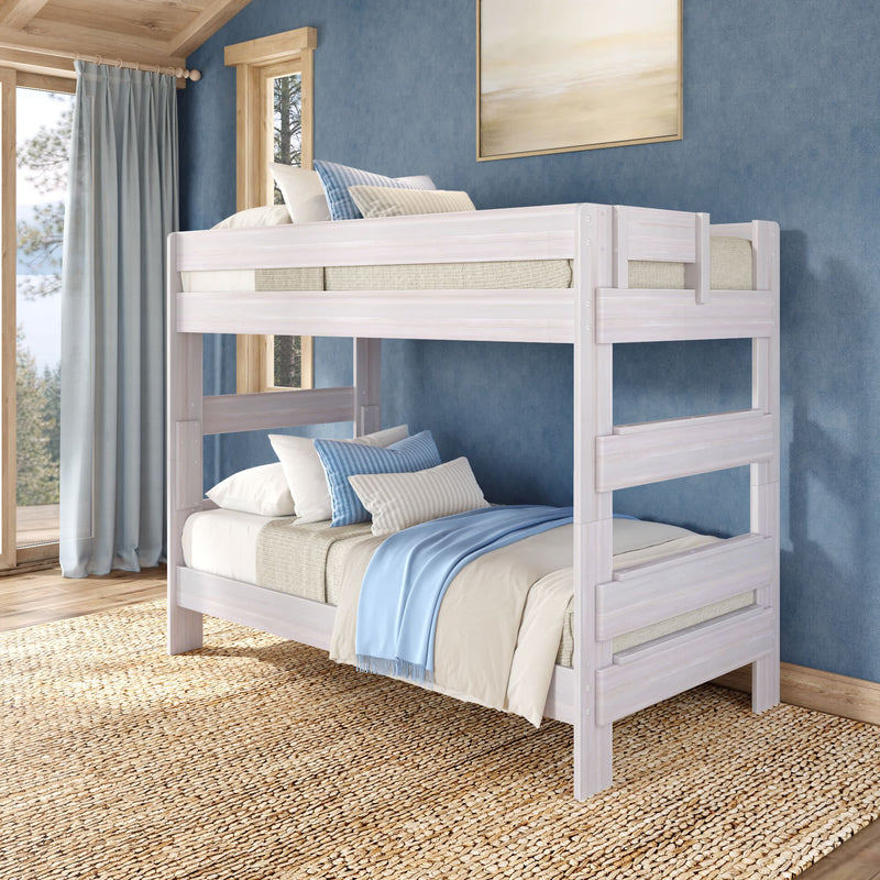 Whitewashed wooden twin-over-twin bunk bed in a coastal-style bedroom with blue walls, light blue and beige bedding, natural jute rug and large windows