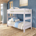 Whitewashed wooden twin-over-twin bunk bed in a coastal-style bedroom with blue walls, light blue and beige bedding, natural jute rug and large windows