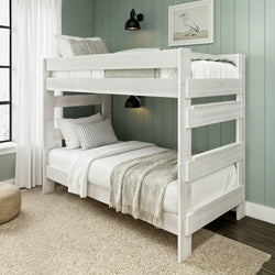 White-painted wooden bunk bed in coastal-style bedroom with sage green shiplap wall, neutral linens and knitted throw, black wall sconces, framed bird art and jute rug