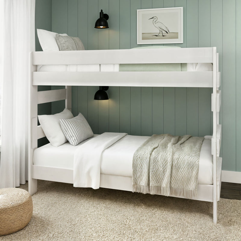 White wooden bunk bed in coastal bedroom with sage green shiplap wall, neutral linens and textured throw, black wall sconces, framed heron artwork and woven pouf on beige carpet