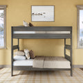 Gray wooden bunk bed in a cozy yellow bedroom with beige bedding and patterned throw pillows, framed lakeside wall art above, two windows with pine tree views and a neutral plaid area rug