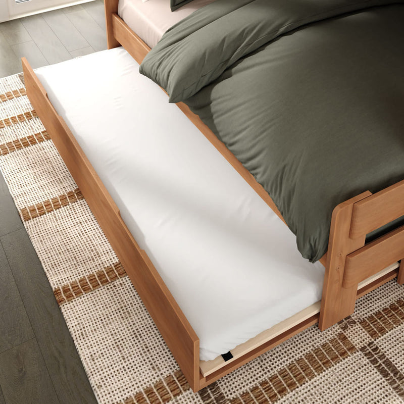 Modern light-wood twin trundle bed with pull-out white trundle mattress, green duvet, under-bed storage frame and woven area rug in a contemporary bedroom