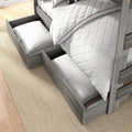 Gray wood twin bunk bed with open under-bed storage drawers holding pillows and white quilted bedding on a beige rug
