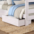 White wooden bunk bed with trundle drawer styled with beige bedding, striped pillows and a light blue throw on a woven jute rug