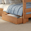 Natural wood trundle bed with pull-out storage drawer, cozy blue woven throw blanket, white sheets and beige pillows on a textured woven rug