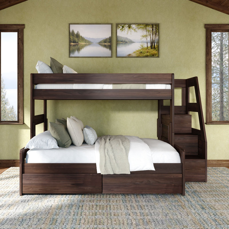 Dark wood twin-over-full bunk bed with staircase and storage, cozy neutral bedding against a green accent wall, framed lake landscape prints and large windows with pine tree views