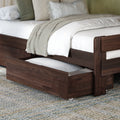 Dark wood trundle bed with white quilted bedding, green accent pillows and beige textured throw, open under-bed storage drawer on gray area rug