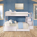 White wooden bunk bed with beige bedding and blue throw against a blue textured wall with framed coastal art, natural wood windows, and woven jute rug