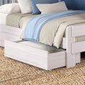 Close-up of light wood storage trundle bed with neutral bedding, pale blue throw blanket, striped accent pillows and woven jute rug