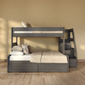 Gray wooden bunk bed with built-in stair storage, neutral beige bedding and patterned pillows in a sunlit modern bedroom with hardwood floor
