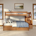 Sunlit modern rustic wooden bunk bed with staircase and built-in storage drawers, layered neutral pillows and blue throw blanket in a cozy bedroom with framed lakeside wall art and large windows.