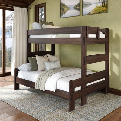 Dark walnut solid wood full-over-full bunk bed in cozy cabin-style bedroom with white linen bedding, layered throw pillows, textured rug and large windows overlooking a forest lake.
