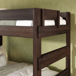 Dark walnut solid wood bunk bed with integrated ladder and safety guardrails, styled with neutral bedding against a textured green bedroom wall