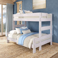 Whitewashed wooden bunk bed in coastal-style bedroom with blue walls, large windows, neutral bedding, blue-striped pillows and jute rug