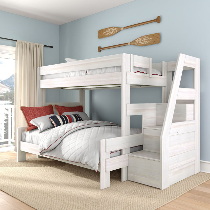 Whitewashed wooden twin-over-full bunk bed with built-in staircase storage, white quilted bedding and red accent pillows in a coastal kids bedroom with oar wall decor and large window