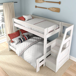 White wooden twin-over-full bunk bed with storage staircase, quilted white bedding and red accent pillows in a coastal kids' bedroom