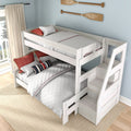 White wooden twin-over-full bunk bed with storage staircase, quilted white bedding and red accent pillows in a coastal kids' bedroom
