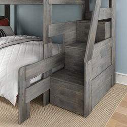 Gray wooden bunk bed with built-in storage staircase and drawers, white quilted bedding on lower bunk in a space-saving kids' bedroom with blue wall and woven rug