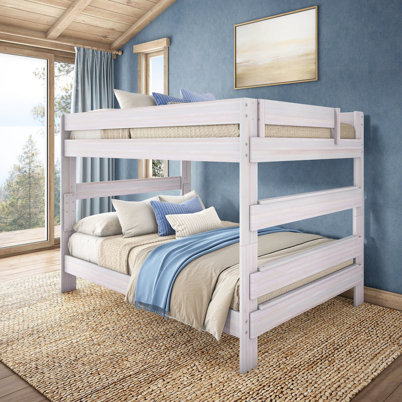 White-washed wooden twin-over-full bunk bed in a coastal bedroom with blue accent wall, layered neutral bedding, large window and jute rug