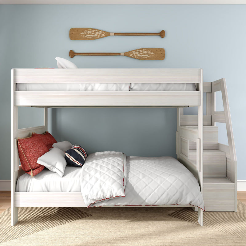 White wooden bunk bed with built-in staircase in a coastal kids' bedroom, light blue wall with wooden oars, white quilted bedding and red accent pillows