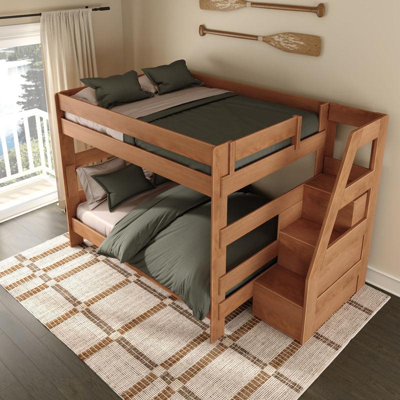 Solid wood twin-over-full bunk bed with built-in storage staircase and green bedding in a coastal-style bedroom with oar wall decor, large window overlooking a lake, patterned rug, and dark hardwood floor