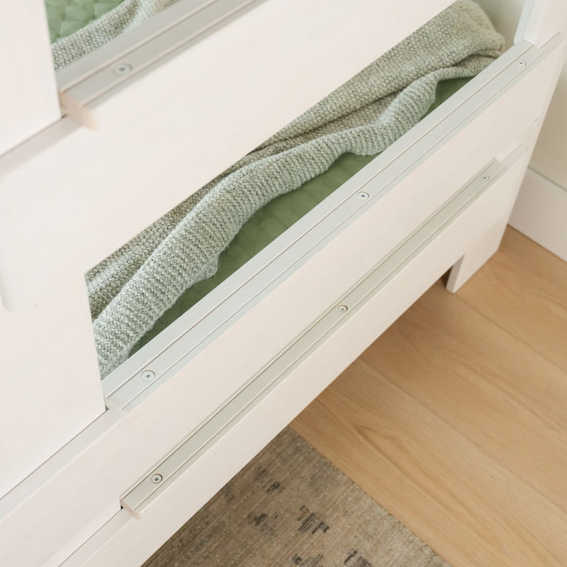 White wooden bed frame with a pull-out drawer containing a green blanket, showcasing under-bed storage solution.