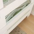 White wooden bed frame with a pull-out drawer containing a green blanket, showcasing under-bed storage solution.