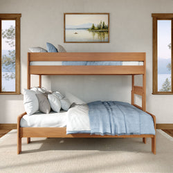 Modern natural wood twin-over-full bunk bed with blue linens and white pillows in a bright lakeside bedroom with large windows and framed art