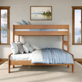 Modern natural wood twin-over-full bunk bed with blue linens and white pillows in a bright lakeside bedroom with large windows and framed art