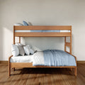 Twin-over-full wooden bunk bed with natural wood finish, light blue bedding and stacked pillows in minimalist bedroom with hardwood floor