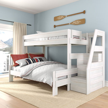 Whitewashed wooden twin-over-full bunk bed with built-in storage staircase in coastal kids' bedroom, white quilt, red pillows, nautical oar wall decor and lake view