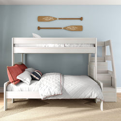 White wooden bunk bed with staircase storage in a coastal kids bedroom, quilted white bedding, red accent pillows and rustic wooden oar wall decor on a light blue wall
