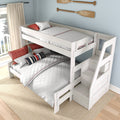 White wooden full-over-twin bunk bed with built-in storage staircase, quilted white bedding and red-navy striped accent pillows in a coastal kids' bedroom with light blue wall and wooden oar décor.
