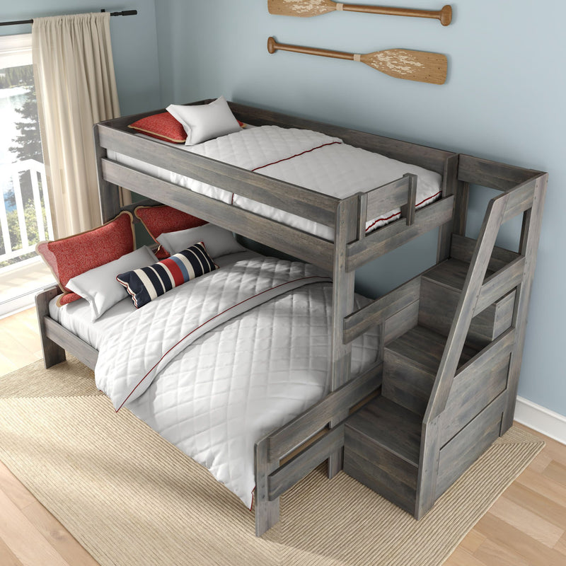 Gray weathered wood twin-over-full bunk bed with built-in staircase storage, white quilted bedding with red piping and red/navy accent pillows in a coastal light-blue bedroom with decorative wooden oars and balcony lake view