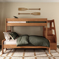 Modern wooden bunk bed with side staircase storage, dark green bedding and pillows in a cozy coastal-style kids’ bedroom with decorative wooden oars on the wall