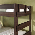 Close-up of a modern dark wood bunk bed frame with built-in guardrails and white bedding against a green textured wall, sturdy twin-over-twin design for kids' bedrooms.