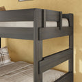 Dark gray wooden bunk bed frame close-up showing guardrails and ladder details against a beige textured wall with neutral bedding and a plaid pillow