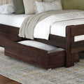 Dark walnut wooden trundle bed with under-bed storage drawer, white quilted bedding, beige knit throw and green accent pillows on textured rug