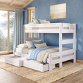 Whitewashed wooden bunk bed with trundle and under-bed storage drawers, layered blue and beige bedding in a coastal-style bedroom with textured blue wall, large window overlooking pine trees and woven jute rug.