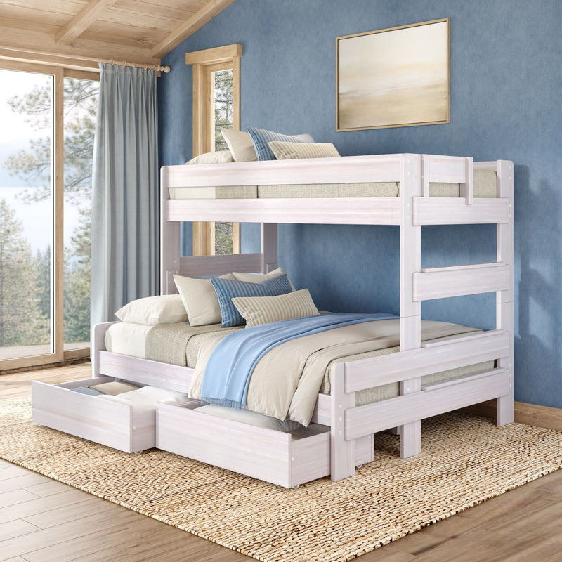 Whitewashed wooden bunk bed with trundle and under-bed storage drawers, layered blue and beige bedding in a coastal-style bedroom with textured blue wall, large window overlooking pine trees and woven jute rug.