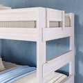 Close-up of whitewashed wooden bunk bed with safety rails and ladder, twin mattresses with blue bedding in a modern kids' room