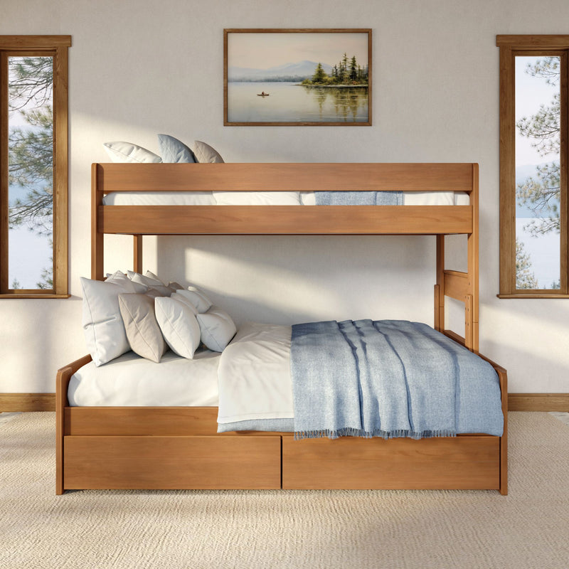 Cozy modern rustic bedroom with a wooden bunk bed and storage drawers, blue throw blanket and layered pillows, framed lake painting and tall windows overlooking pine trees