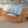 Wooden trundle bed with light blue woven throw blanket, white linens and under-bed storage drawer in a cozy modern bedroom